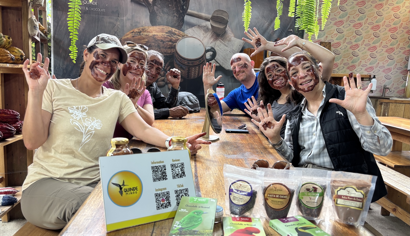 Group of friends sitting at a table with chocolate face masks on, showing their chocolatey hands
