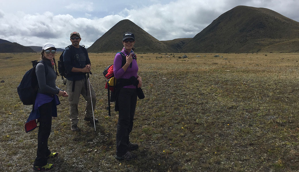 Two ladies and a man in hiking clothes and baseball hats smiling with volcanic mounds in background in Cotopaxi National Park