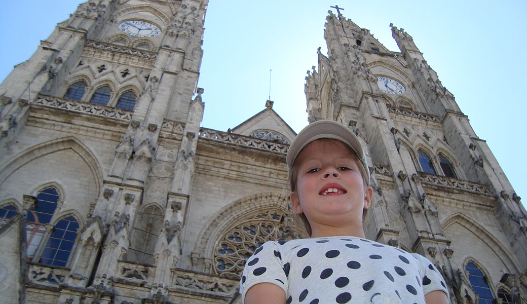 Young girl with spotty t-shirt and baseball cap smiling in front of clock towers of the Basilica in Quito, Ecuador